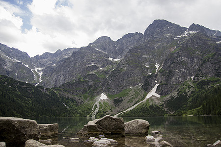 美丽的夏季高山湖景被绿树覆盖 前面有石头 天空中有云彩 山在水中的倒影 水晶般清澈的水 欧洲 阿尔卑斯山反射艺术太阳顶峰公园旅行图片