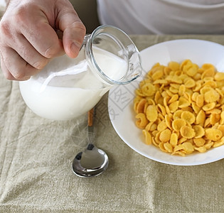 短发男子将牛奶倒入普通粗糙桌布上白盘子里的玉米片中 从上面看 选择性的焦点 概念 简单快速的美式健康早餐活力盘子玉米奶制品谷物食图片
