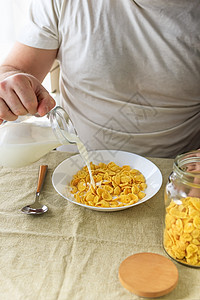 短发男子将牛奶倒入普通粗糙桌布上白盘子里的玉米片中 从上面看 选择性的焦点 概念 简单快速的美式健康早餐玉米厨房盘子谷物男性学士图片