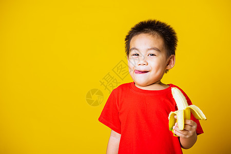 穿着红色T恤运动的笑容 可爱可爱的小男孩婴儿食物香蕉育儿营养水果幸福乐趣孩子快乐图片