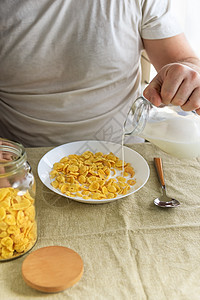 短发男子将牛奶倒入普通粗糙桌布上白盘子里的玉米片中 从上面看 选择性的焦点 概念 简单快速的美式健康早餐烹饪学士奶制品营养盘子桌图片