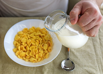 短发男子将牛奶倒入普通粗糙桌布上白盘子里的玉米片中 从上面看 选择性的焦点 概念 简单快速的美式健康早餐烹饪活力男性奶制品盘子厨图片