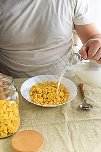 短发男子将牛奶倒入普通粗糙桌布上白盘子里的玉米片中 从上面看 选择性的焦点 概念 简单快速的美式健康早餐烹饪学士男人厨房谷物营养图片