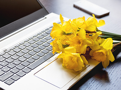 装在银金属笔记本电脑上的Narcissus或水仙 手提装置上的亮黄色花朵 木制背景的智能手机桌子互联网水仙花技术工作职场商城花瓣背景图片