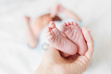 母亲拿着新生婴儿的赤身高跟鞋 小脚在女人手里 在家很舒服儿子家庭手指蓝色女士妈妈白色脚跟父母投标图片