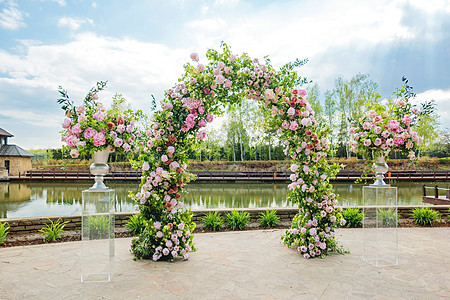 美丽的花岗拱门用于婚礼仪式 有粉红玫瑰和风味的花瓶 在池塘附近的公园外布置婚纱植物群植物大厦牡丹衬套玫瑰婚姻配饰日落庄园图片