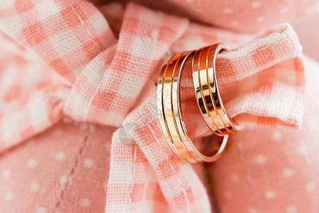 金婚戒指贴在粉红色格子织物上 结婚珠宝的细节背景图片