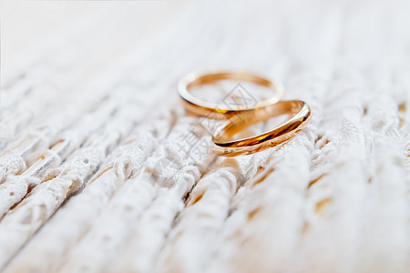 对花边织物上的金色结婚戒指 婚礼刺绣礼服细节浪漫宏观庆典珠宝婚姻装饰品裙子蕾丝金子白色背景图片