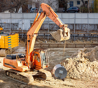 城区住宅楼中一个有围栏的建筑工地上建造了一个重型爬行式挖土机工程项目背景图片