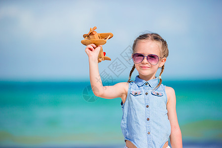 带着玩具飞机的快乐小女孩 在白沙滩上手握着玩具飞机航班乐趣运输动机假期活动旅行游戏黄色航空图片