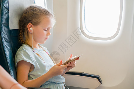 可爱的小孩 在飞机窗户旁边有笔记本电脑的孩子 Coote kid座位闲暇旅游耳机游客染色玩具沙龙童年电影图片