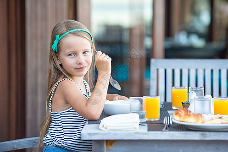 可爱的小女孩在户外咖啡厅吃早餐孩子橙子咖啡店快乐餐厅水果瓶子假期小吃杯子图片
