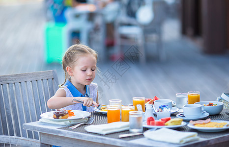 可爱的小女孩在户外咖啡厅吃早餐餐厅孩子女儿金发蜂蜜婴儿杯子快乐水果食物图片