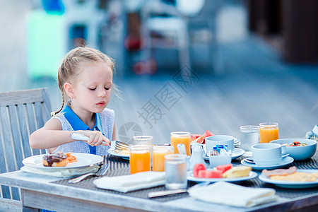 可爱的小女孩在户外咖啡厅吃早餐餐厅快乐婴儿孩子咖啡店水果食物桌子金发杯子图片