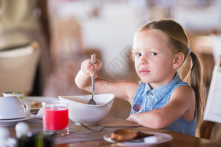吃芒果小女孩可爱的小女孩在户外咖啡厅吃早餐水果女儿餐厅金发西瓜食物瓶子桌子橙子杯子背景