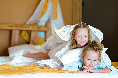 可爱的小女孩在家床上玩得开心女孩阳光父母孩子白色乐趣拥抱女性孩子们姐姐图片