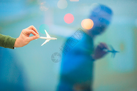 在机场背景大窗口上拿着飞机模型玩具的近身手举着一个机型玩具图片