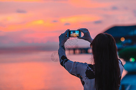 女人在她美丽的日落的手机上拍照旅行椰子橙子照片场景假期棕榈闲暇天堂电话图片