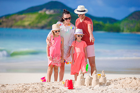 四个家庭在热带白沙滩建沙丘城堡母亲海岸线海洋游泳衣沙堡童年女儿男人海岸情调图片