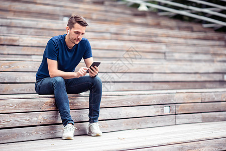 男人在公园散步时正在看手机上的短信 而男子则在公园里走动连接新闻4g大学耳机用法拿铁游客应用程序娱乐图片
