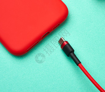 绿色背景的纺织品编条纹中的红色智能手机和电缆高清图片