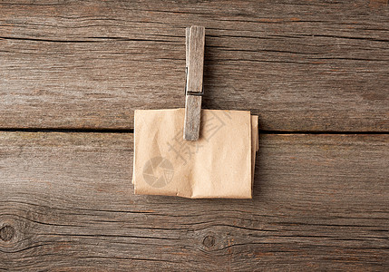 灰色木质背景上的木制衣夹和折叠的棕色纸图片