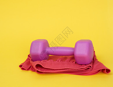 黄色背景的粉红色塑料哑铃(一公斤)图片