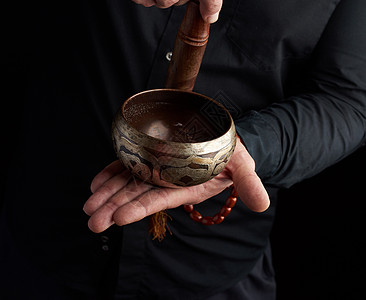 穿黑衬衫的男人在铜铁板周围旋转木棍宗教仪式冥想佛教徒音乐杯子手印金属治疗活力背景图片