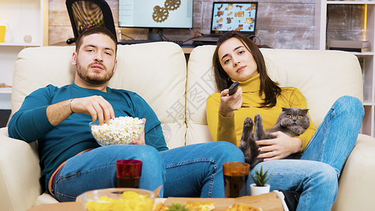 无聊女孩坐在沙发上 猫在她腿上宠物电影男人女士房子爆米花房间娱乐公寓电视节目图片