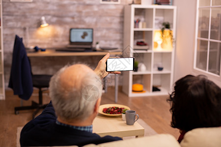 老年退休夫妇的后视镜 看着一个带白色隔离屏幕的智能手机成人女性老年人快乐沙发小样微笑丈夫女士技术图片