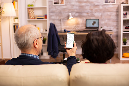 老年退休夫妇的后视镜 看着一个带白色隔离屏幕的智能手机男人沙发互联网老年人小样成人微笑技术快乐阅读图片