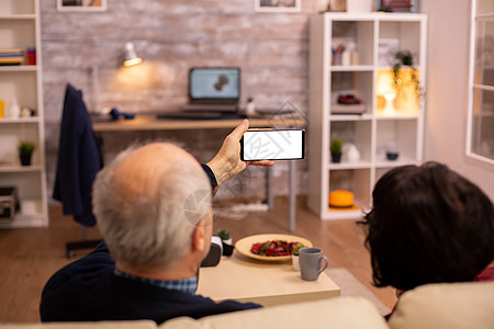 老年退休夫妇的后视镜 看着一个带白色隔离屏幕的智能手机小样老年人快乐微笑互联网成人阅读丈夫沙发技术图片