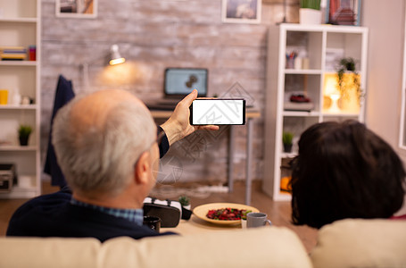 老年退休夫妇的后视镜 看着一个带白色隔离屏幕的智能手机微笑技术互联网阅读女性沙发小样老年人老夫妻成人图片