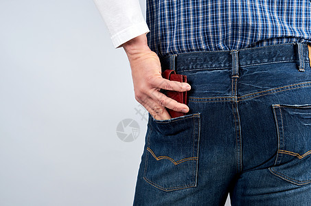 穿着蓝色格子衬衫和牛仔裤的男人将皮衣钱包放进他的图片