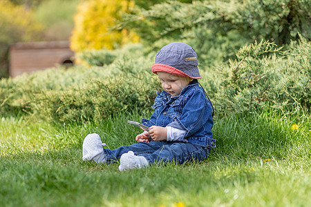 小小宝贝男孩坐在户外 拿着智能电话图片