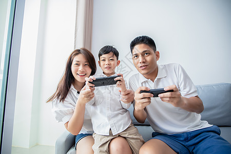 亚洲家庭一起玩电脑游戏很开心 父子有手机控制器 母亲在家里为玩家加油儿子房间男人爸爸父亲技术女孩女性游戏安慰图片
