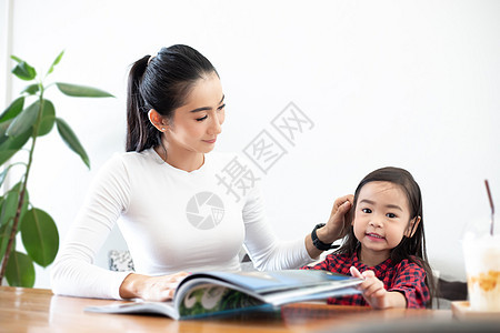 亚裔母亲正在教女儿在T期间读一本书成人快乐房间沙发女性家庭妈妈教育学习客厅图片