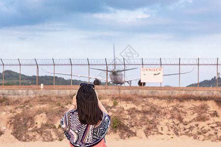 美丽的女人的画像正在拍摄飞机起飞降落在跑道轨道上的照片 旅游妇女在机场围栏旁玩摄影车飞机 旅行危险图片