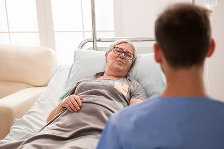 在养老院与男医生交谈时躺在床上的老女人住宅药品疾病照顾者护士护理医院老年疗养院医疗高级的高清图片素材