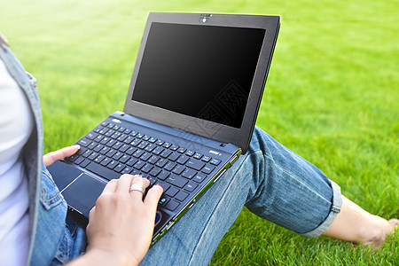 近距离观察女性坐在公园的绿草上 腿上放着笔记本电脑度过夏日户外工作 使用笔记本电脑和无线互联网进行在线工作 空白屏幕图片