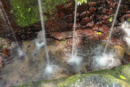 的圣水泉 巴厘岛 印度尼西亚 水落在水面上 喷洒在岩壁上的苔藓和热带植被上图片