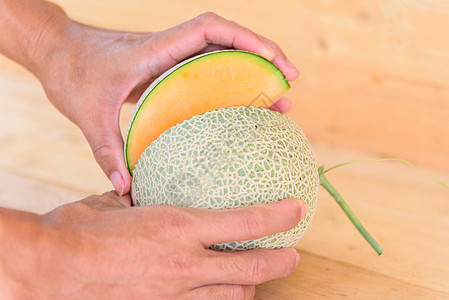 男子用刀把橙色瓜子在木板上分割开来营养橙瓜盘子食物饮食甘露水果热带绿色西瓜图片