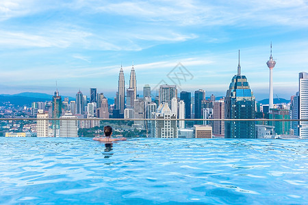 马来西亚城市女性在无限游泳池顶顶顶顶上放松 看着美丽的城市摩天大楼观望着马来西亚的Kala plumur背景