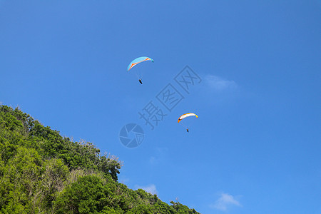 在天空中滑翔伞 两个单人滑翔伞在阳光明媚的日子里飞越热带巴厘岛 绿松石背景上的美丽滑翔伞 积极的生活方式和极限运动的概念跳伞享受图片