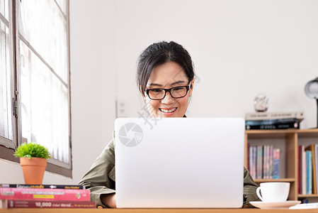 现代亚洲年轻女性在家工作时充满快乐和微笑眼镜房间人士书架电脑咖啡内阁商务女士技术图片