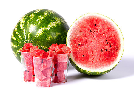 在新鲜有机绿色西瓜前面的塑料杯中切成红色西瓜块 并切成一半具有红色质地的西瓜图片