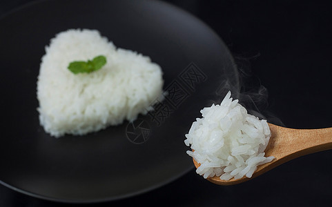 勺子上加烟的热煮茉莉米饭 黑碗上的大米心脏形状作为背景厨房耳朵美食溪流服务饮食餐厅粮食煮沸生活图片