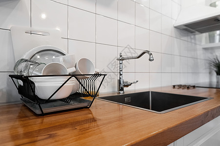 碗碟架可在木制台面 白色墙砖 水槽和水龙头上放置许多碗碟和杯子 现代斯堪的纳维亚厨房带排水板的经济型轻型抗菌洗碗机盘子刀具器皿商图片