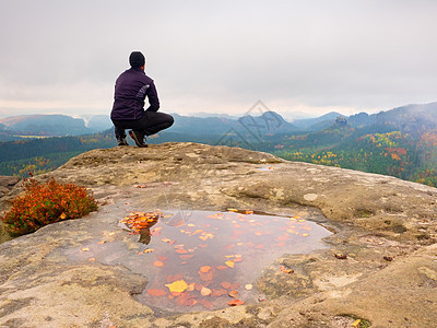 黑色的观光客坐在悬崖边缘 寻找迷雾山丘山谷爬坡风衣旅行成就远足者秋雾享受岩石天空黄色图片
