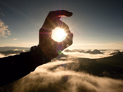 人手触碰太阳 在美丽的山丘中弥漫的白昼男人射线烟雾天空手触真菌反转公园山峰阳光背景图片